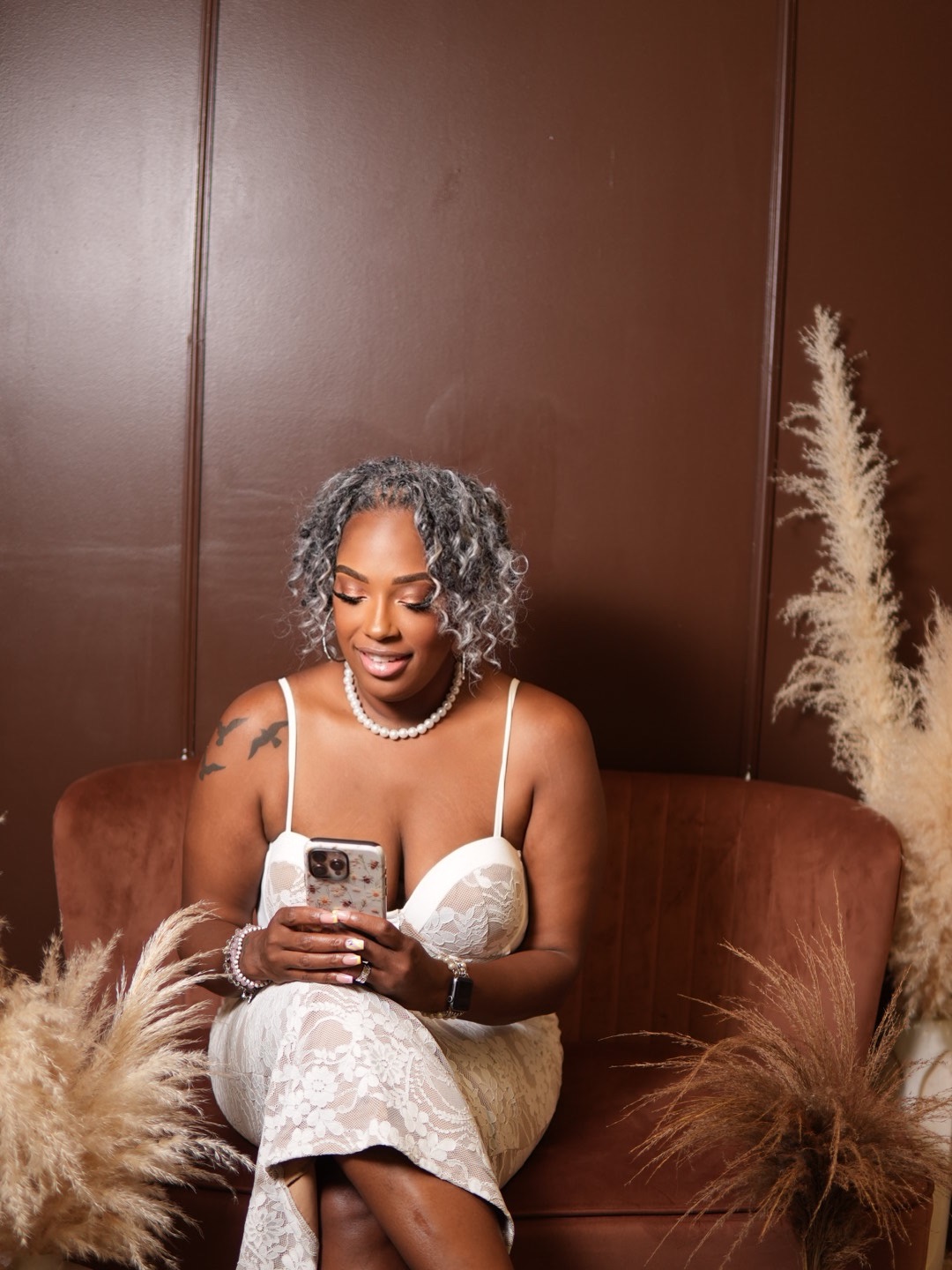 B. Johnson-Gray seated on a brown sofa in a white lace dress reviewing content on her phone